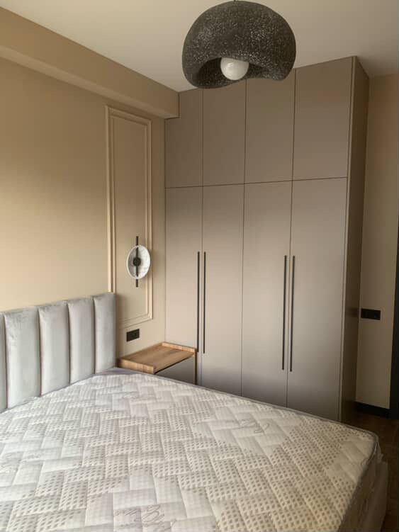 Modern minimalist bedroom with a built-in wardrobe, padded headboard, and neutral color tones | თანამედროვე მინიმალისტური საძინებელი ჩაშენებული ტანსაცმლის კარადით, რბილი თავის საკიდით და ნეიტრალური ფერებით